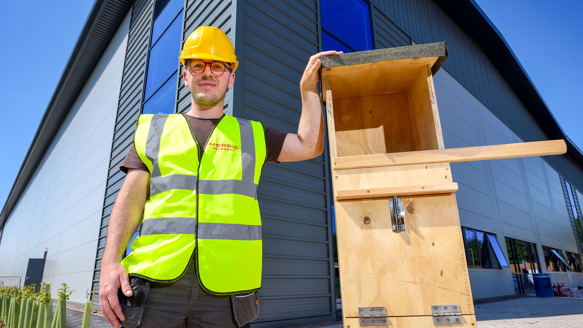 A man from Morris Joinery stands beside an owl box designed for Hortonwood 45, showcasing craftsmanship and design.